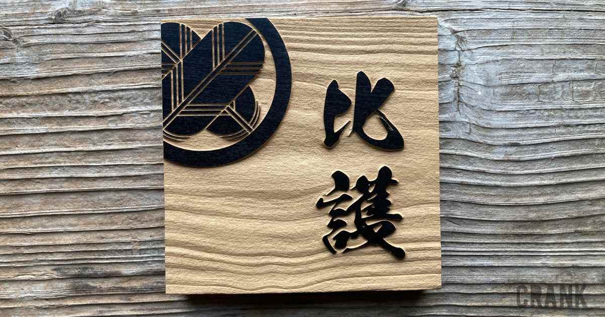 木製表札に黒い家紋と漢字の筆文字が浮き彫り加工されたデザイン