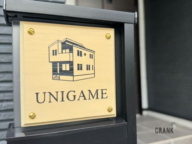 CRANKのオーダーメイド木製表札「ご自宅の外観を表札へ」。雲丹亀ご一家の自宅外観が彫刻され、「UNIGAME」の文字と真鍮ネジが見えるアップ