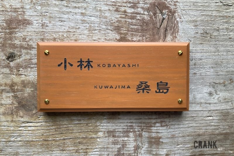 アコヤ材を使用した二世帯住宅用の木製表札。真鍮ネジとチェリーカラーの仕上げ。