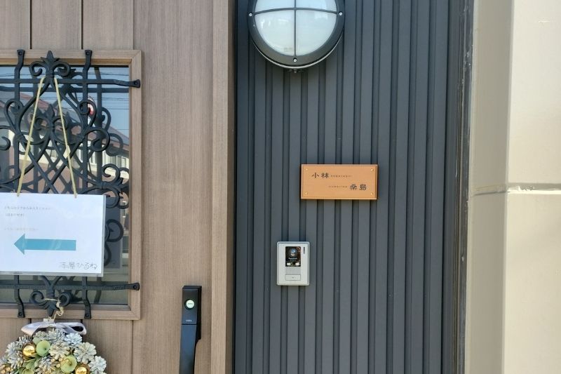 玄関ドアの横に設置されたアコヤ材の二世帯住宅用木製表札