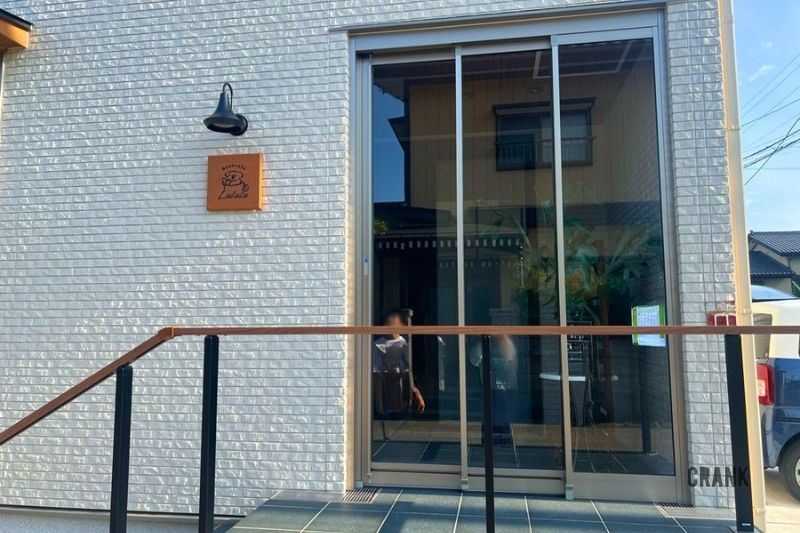 白いタイルの外壁とブラケットライトに映えるBookcafe Lululu様のオーダーメイド木製店舗看板